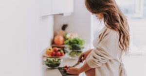 Mujer cocinando verduras en cocina blanca